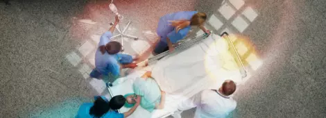 Three nurses and one doctor pushing one patient in a bed in hospital corridor