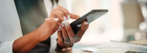 woman at desk with laptop, holding and using her smartphone