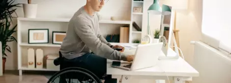Young man in a wheelchair working on his laptop at his desk