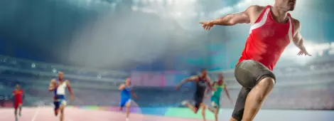 Male track athlete sprinting over the finish line of a race with his arms outstretched in victory