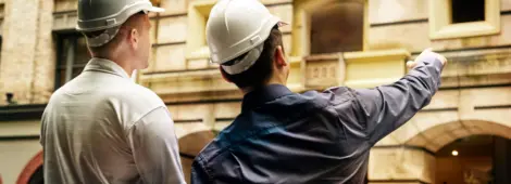 Two engineers in white hard hats pointing at a building