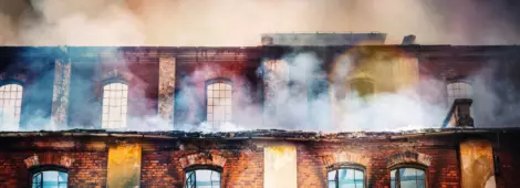 Photo of a burning old red-brick factory with a lot of smoke.