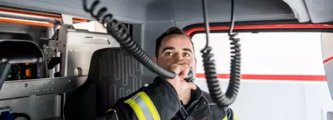 Male firefighter in the driver's seat of a fire truck using the handheld radio