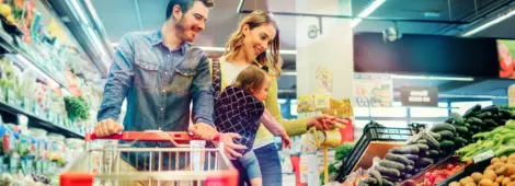 Happy couple with a baby pushing a shopping cart in a grocery store