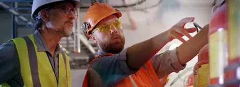 Bearded worker demonstrating fire extinguishers to mature inspector while working on power station