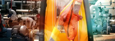 A worker in an orange hazmat suit exits an inflatable decontamination tent at an industrial facility