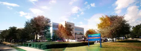 Modern building and parking lot under a partly cloudy sky. Lush trees surround the area.