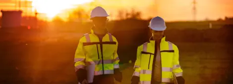 Two engineers discussing while walking on rural field during sunset
