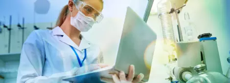 confident young female scientist in protective mask and safety goggles using laptop