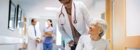 A female doctor pushing a senior patient on a wheelchair in a hospital, smiling at each other