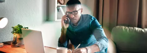 young businessman sitting alone in his office and talking on his cellphone while making notes