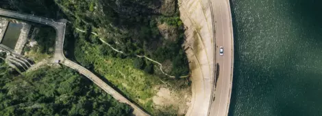Aerial shot of a road that is next to a body of water and some foliage