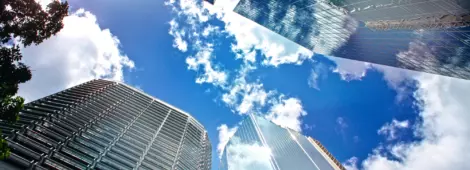 View looking up at blue cloudy sky through skyscrapers reflecting clouds and other buildings