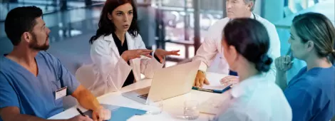 Three doctors and two nurses sitting at a table having a discussion, all have their own notebook