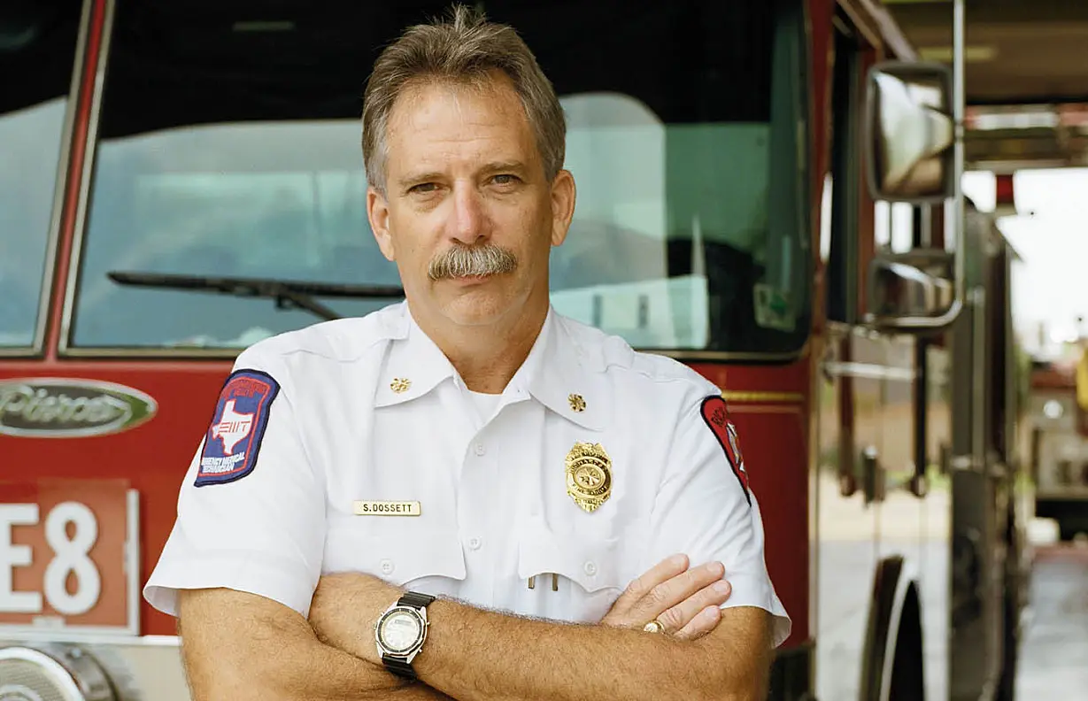 male firefighter with arms crossed standing in front of a red fire truck