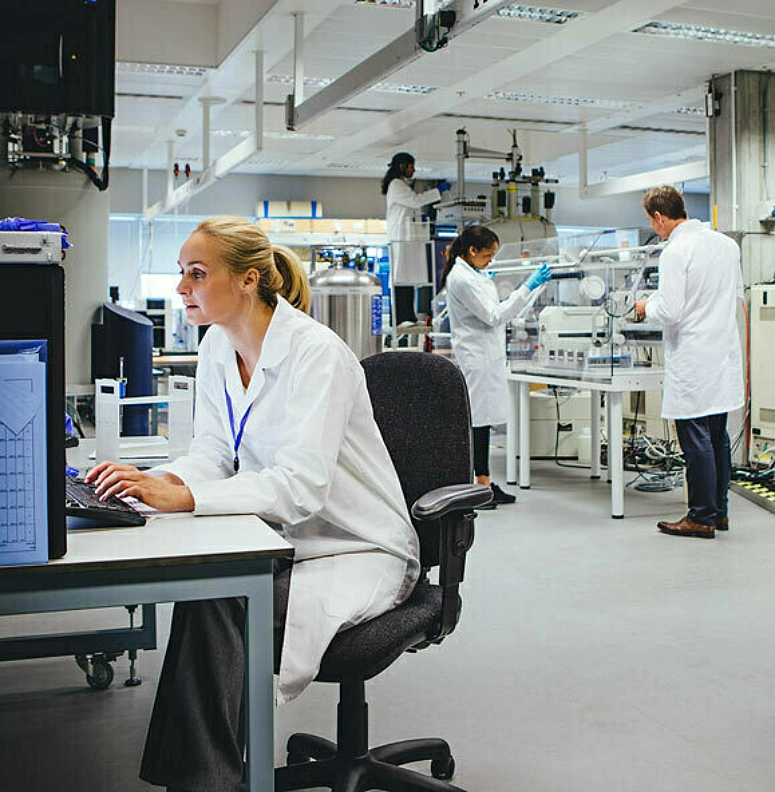 Woman in white coat types on keyboard with other workers in background