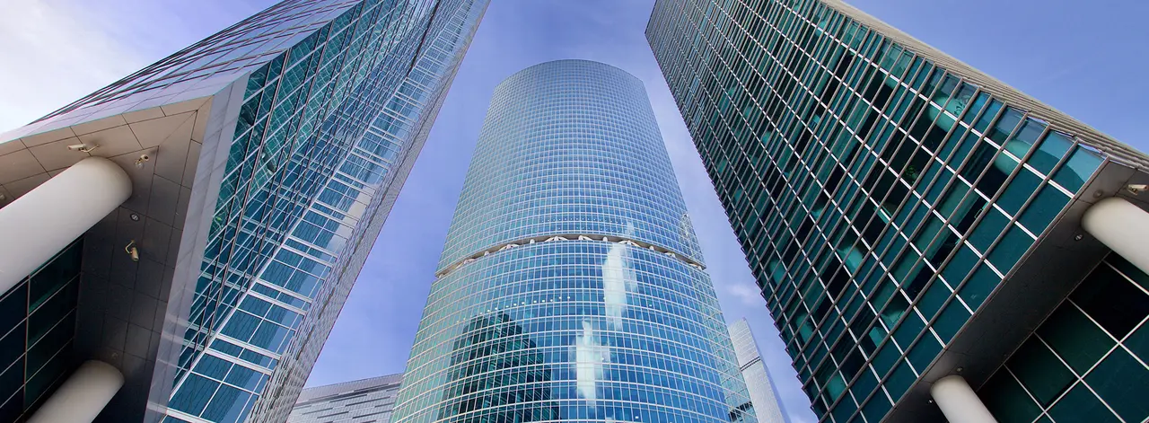 Looking up at glass-clad commercial office towers against a blue sky