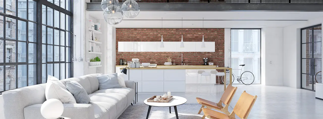 Bright open loft with a white sectional sofa, exposed-brick kitchen wall and floor-to-ceiling industrial windows