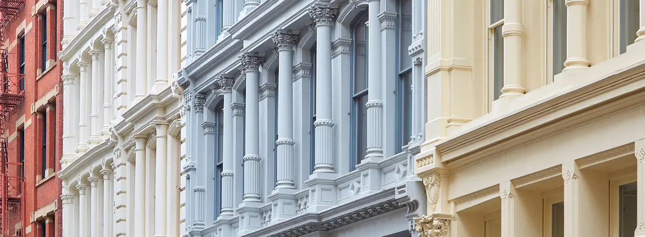 Row of cast-iron and brownstone building facades with tall arched windows in New York City