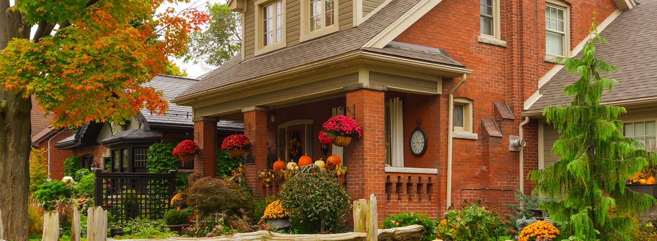 Red brick home with a covered porch, fall foliage and potted flowers