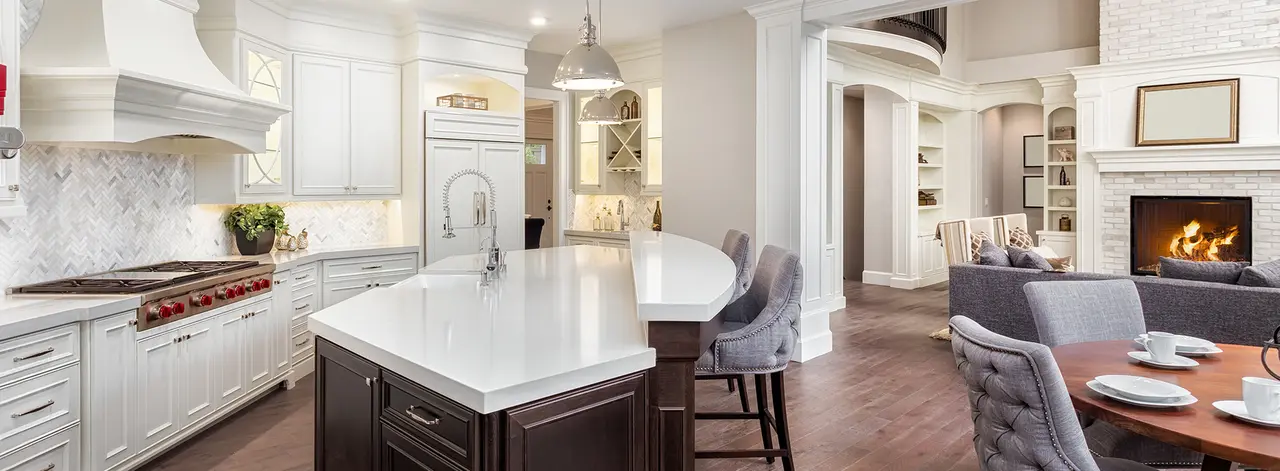 White chef's kitchen with a marble island, bar stools and a fireplace in the adjoining living area