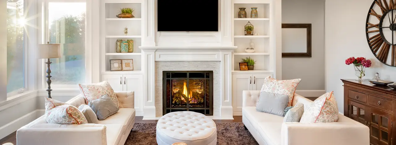 White living room with a lit fireplace, built-in shelving and two cream sofas