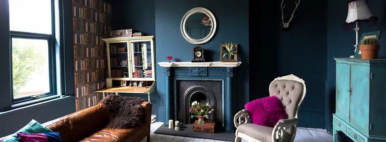 Dark blue living room with a leather sofa, cast-iron fireplace and eclectic vintage furniture