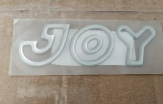 EMBLEMA JOY (PRATA VAZADO)