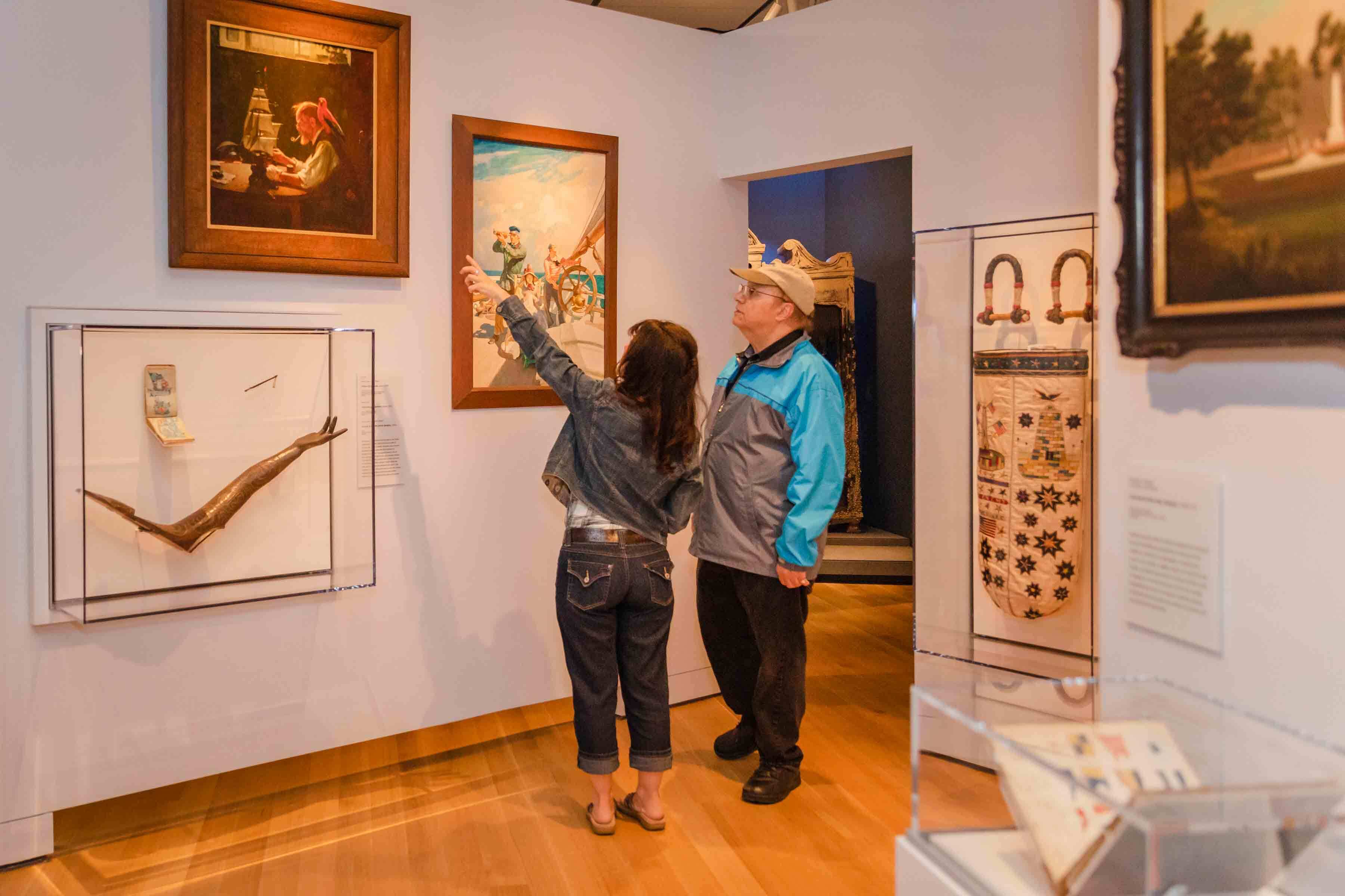 Two visitors in a gallery pointing up and paintings on a white wall