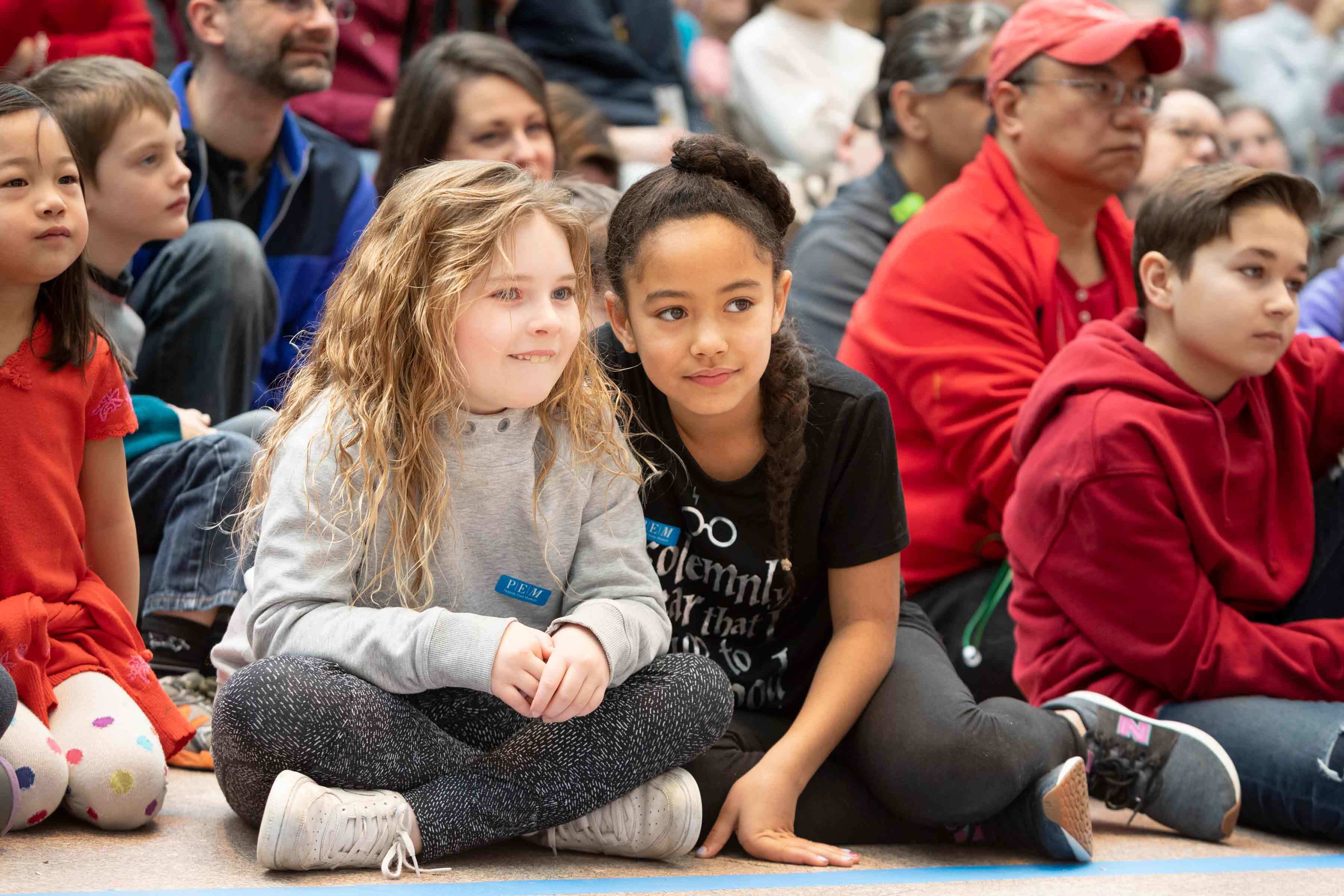 Young children sitting on the floow in a crowd watching the Lunar New Year event dancers