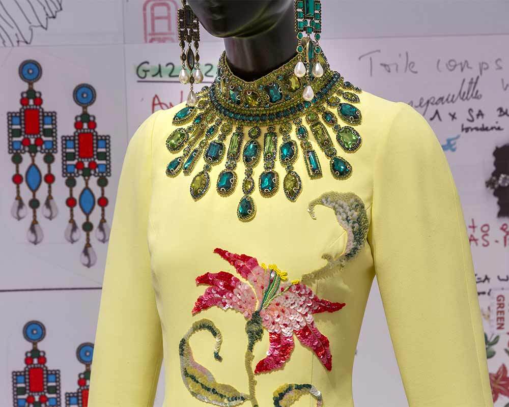 A dress embroidered with a lily, accessorized with a sunburst necklace.