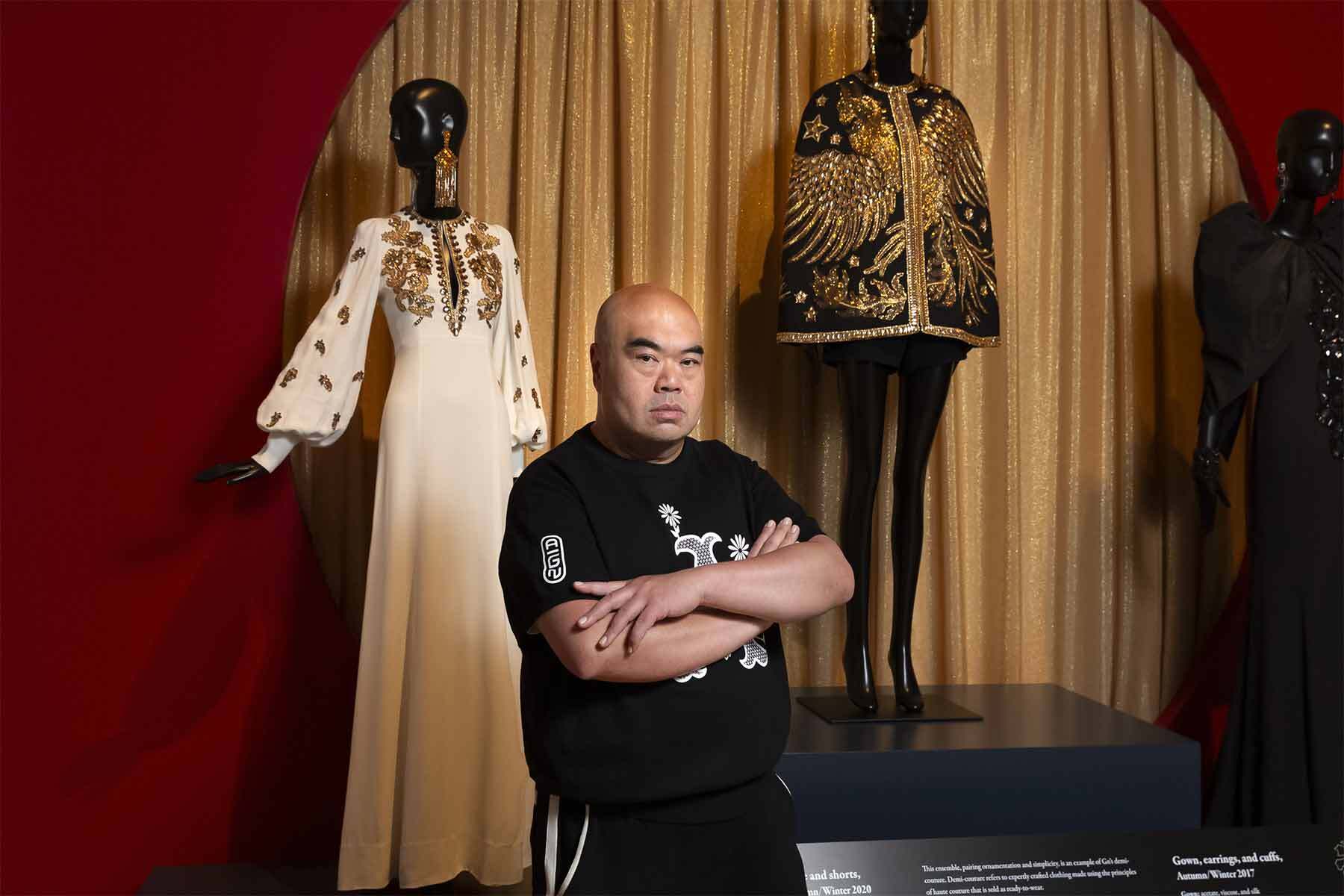 Designer Andrew Gn stands in front of two of his beaded ensembles.