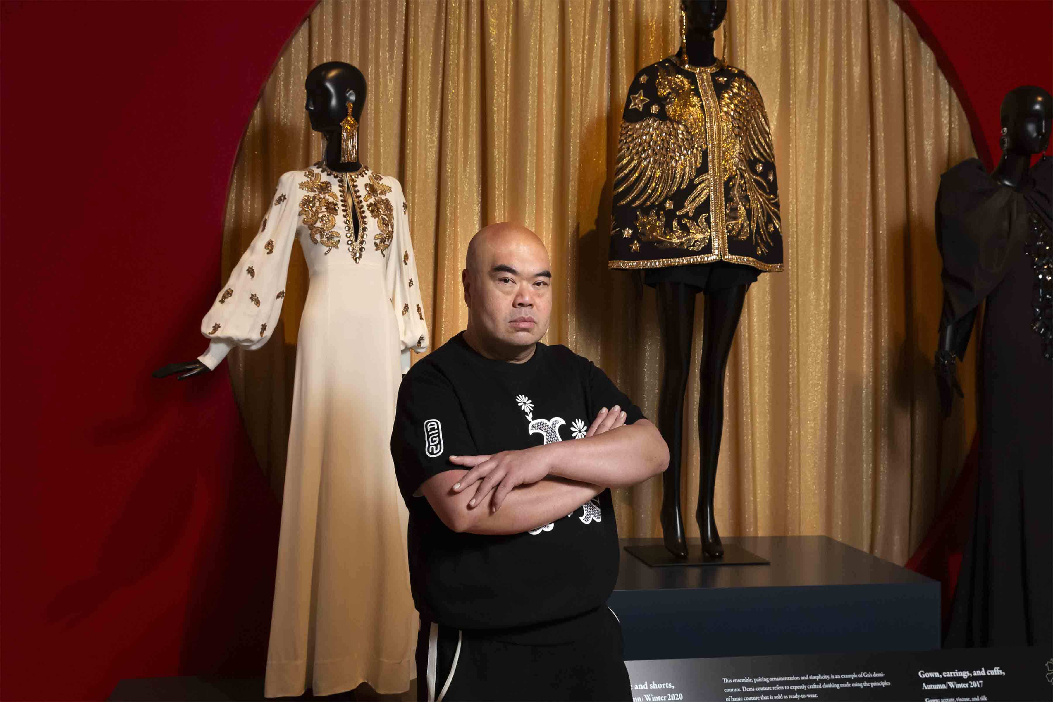 Designer Andrew Gn stands in front of two of his beaded ensembles.