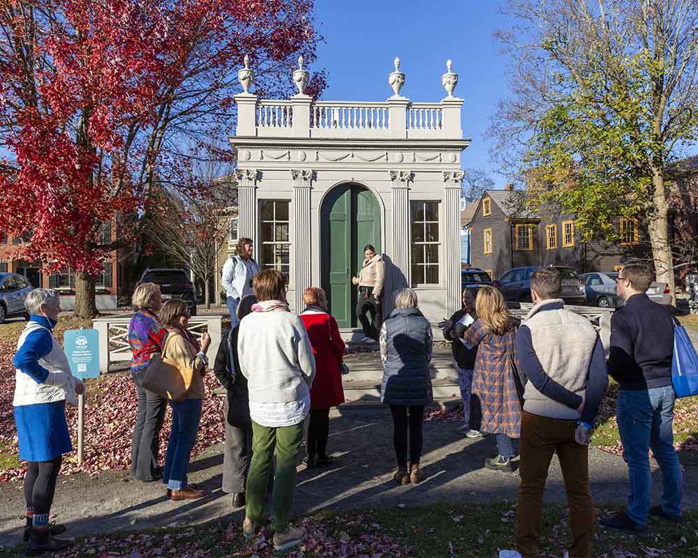 A group of people on a walking tour listening to their guide in front of the Derby-Beebe Summer house.