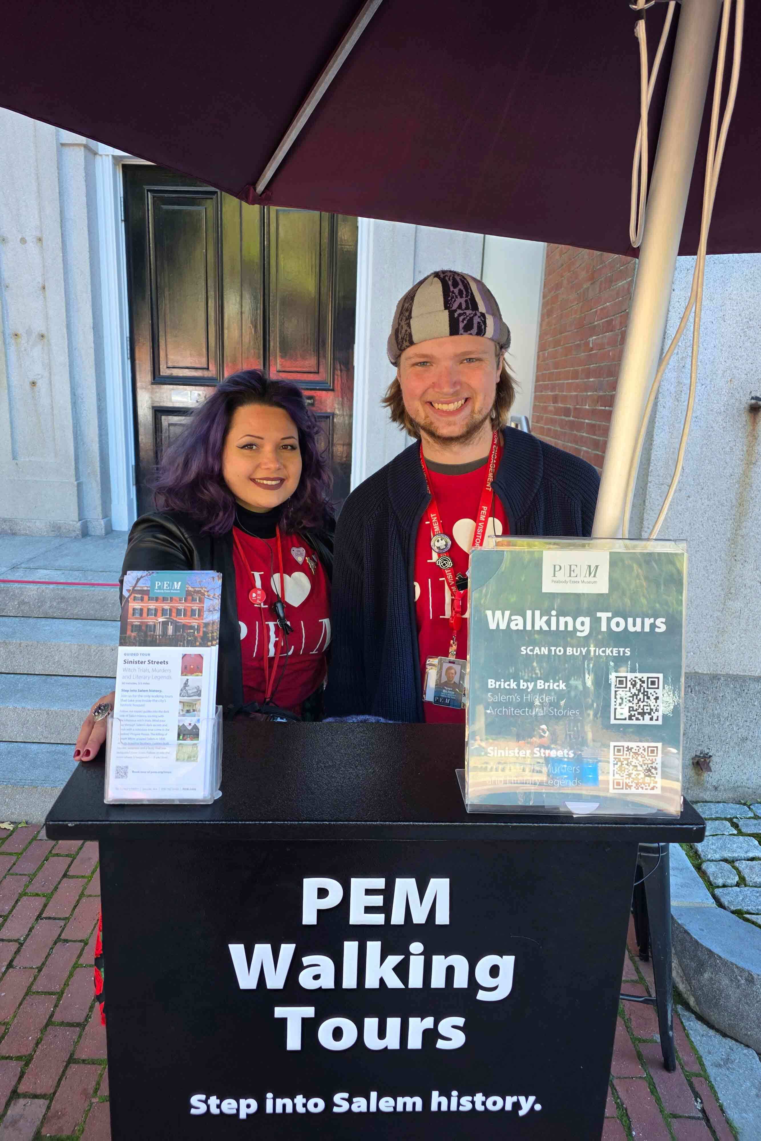 Two smiling tour guides stand behind a podium on PEM's granite steps.
