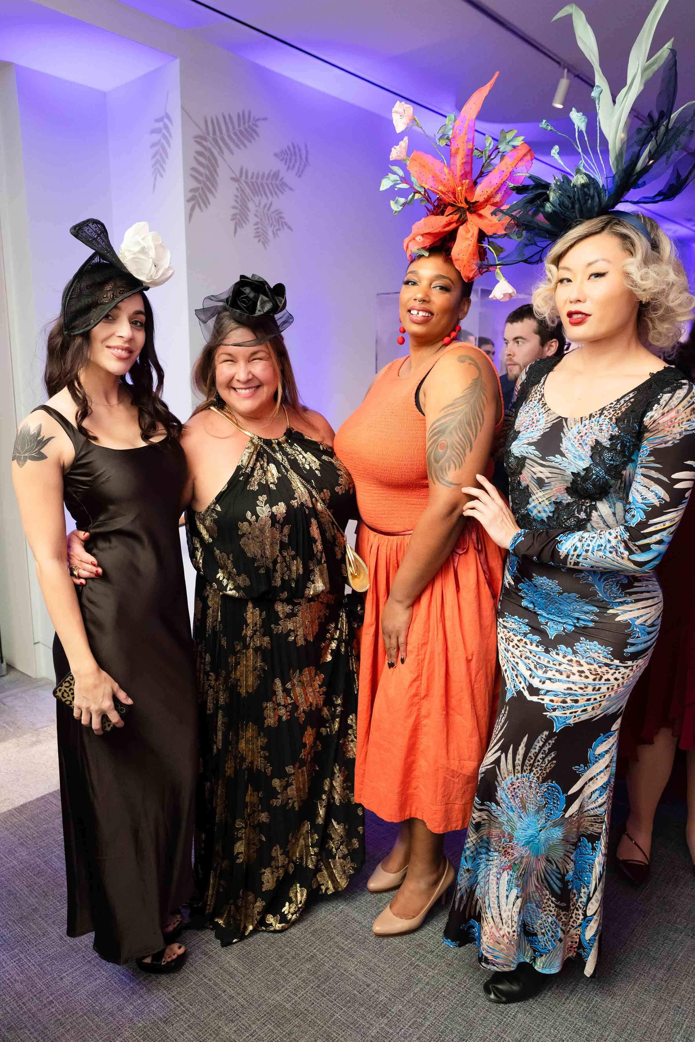 Four smiling women pose in their gowns and dramatic floral fascinators.