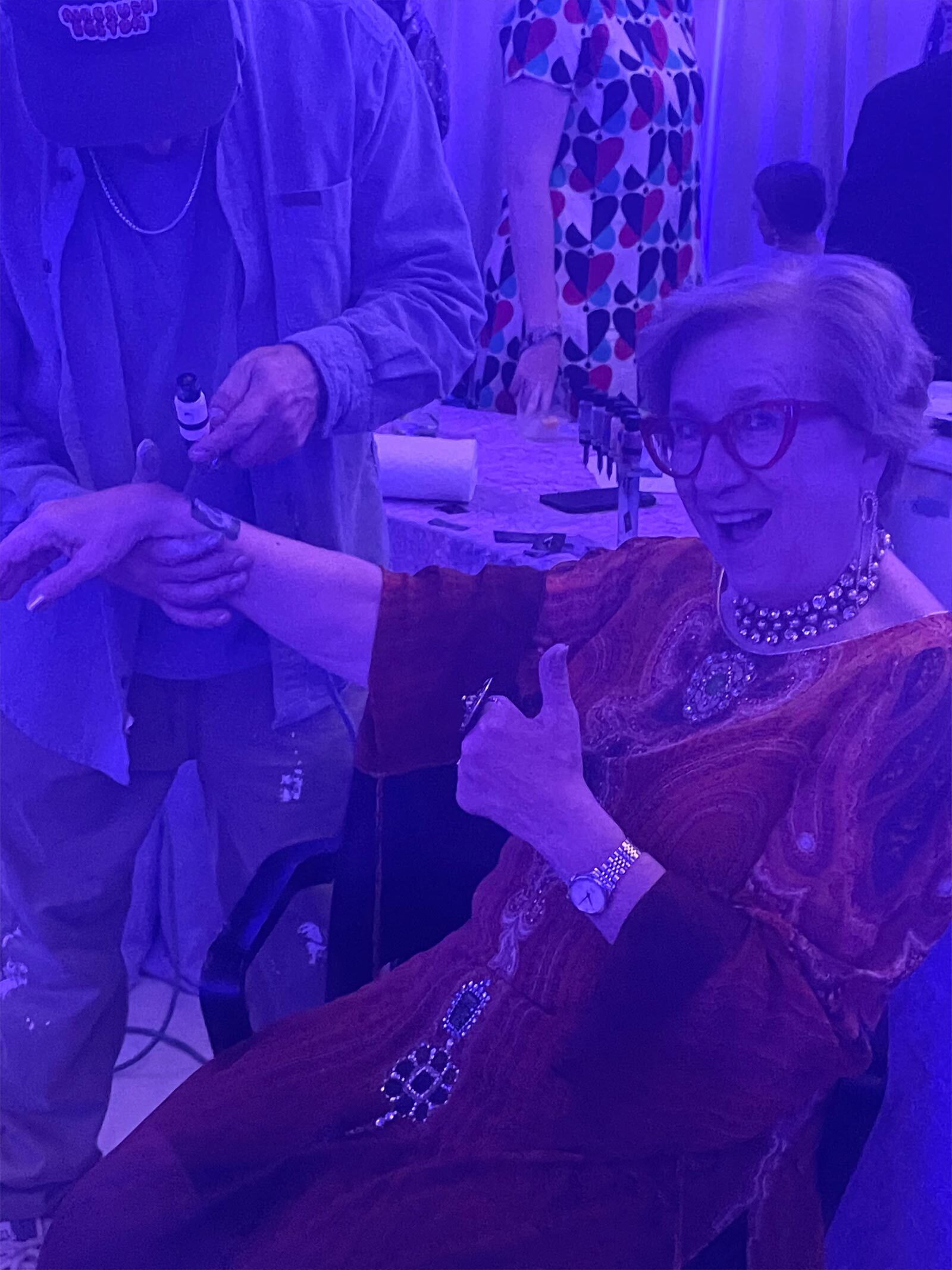 Lynda, wearing her gala gown, gives a thumbs up as she receives an airbrush tattoo on her wrist.