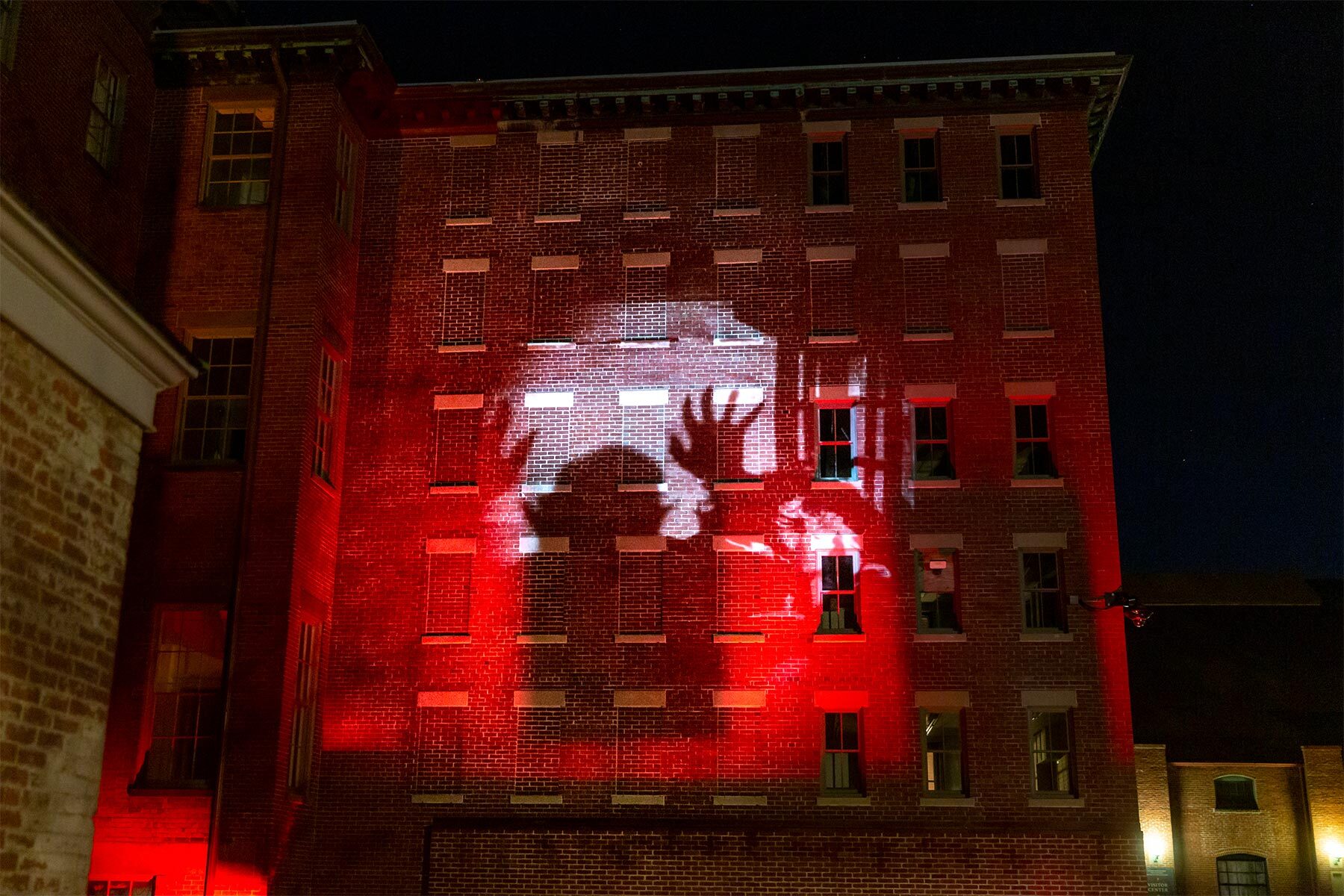 Exterior of a brick building at night with a light projection of the film Nosferatu