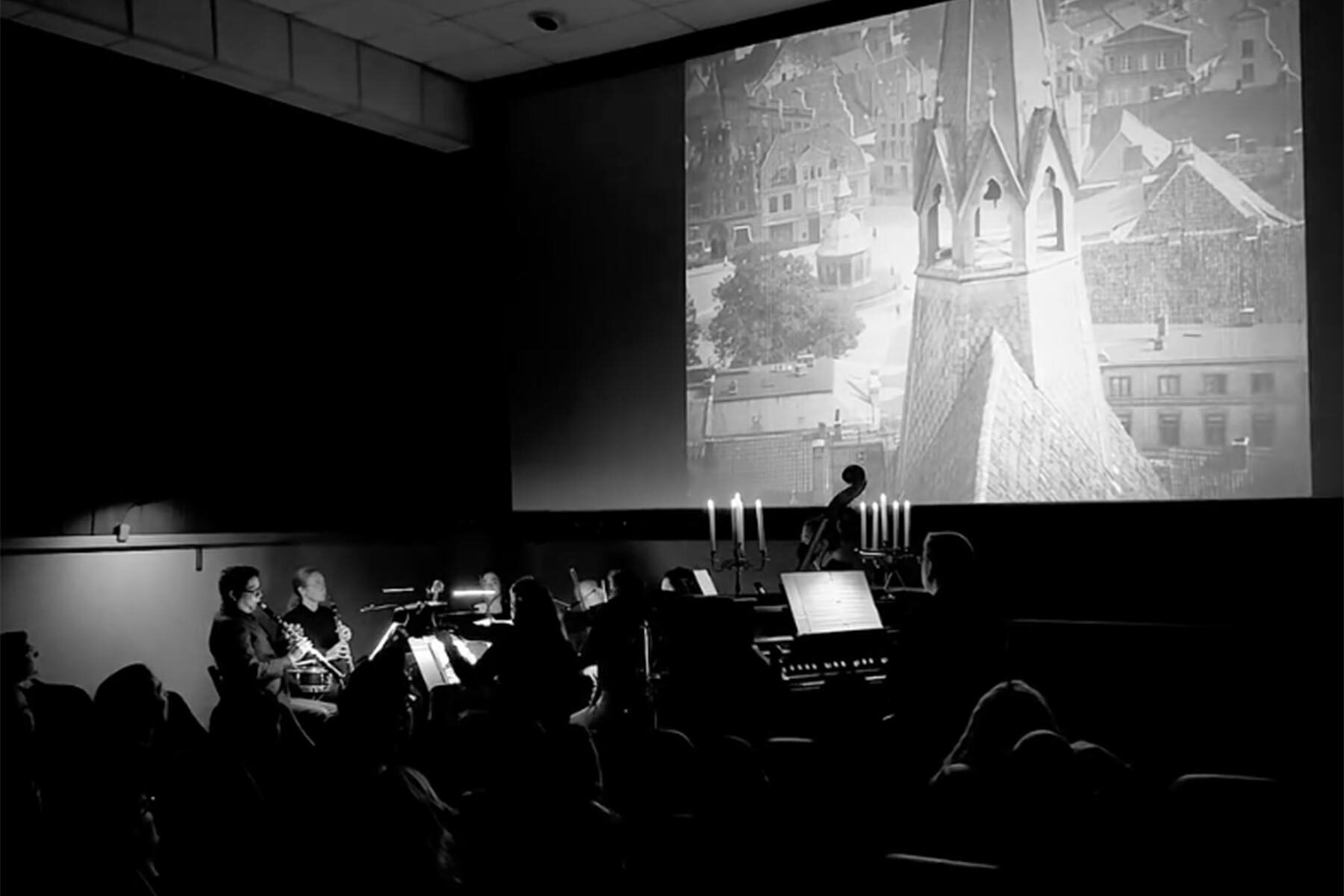 Concert setting with musicians silhouetted in front of a projected black-and-white film scene