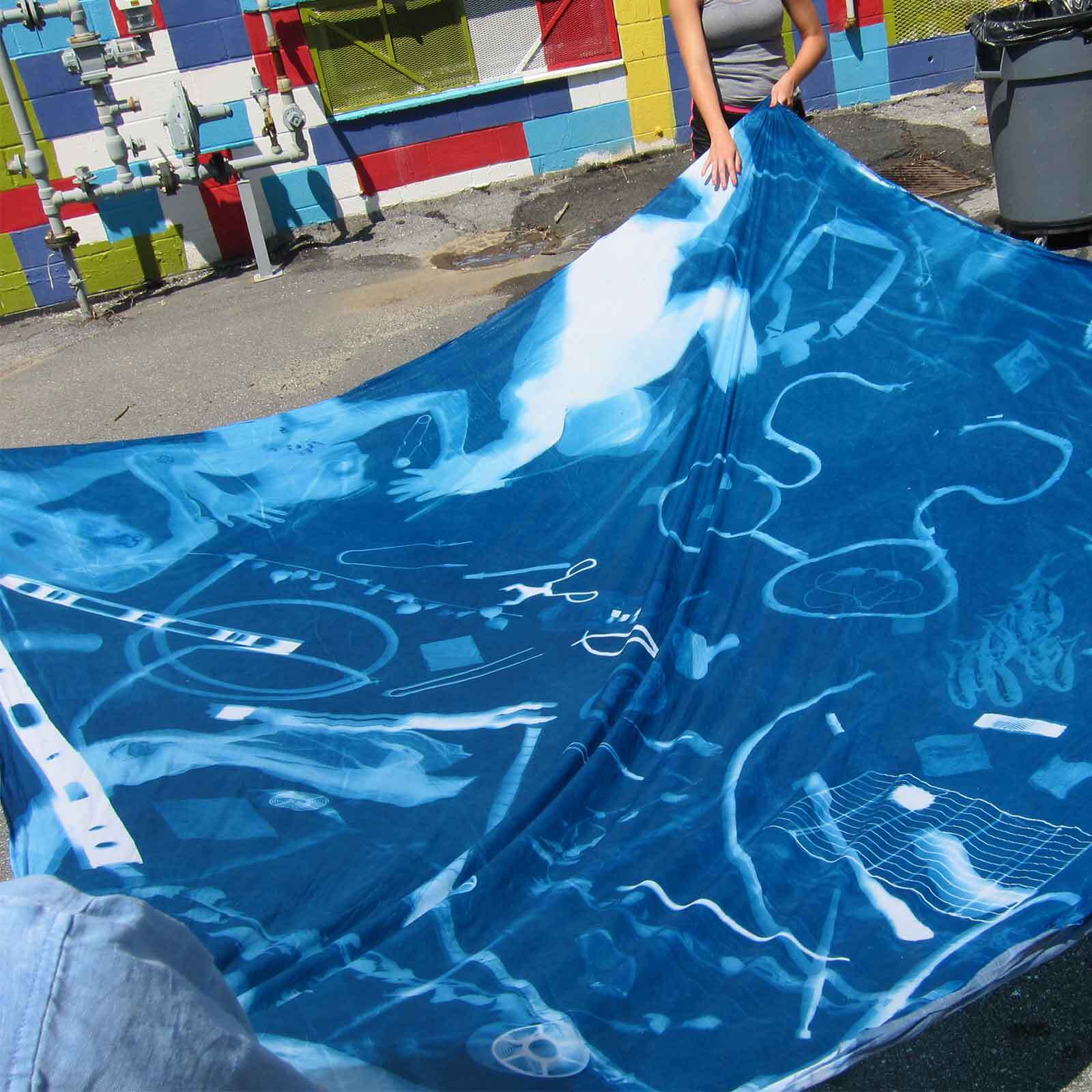 A group of people holding fabric displaying a cyanotype print