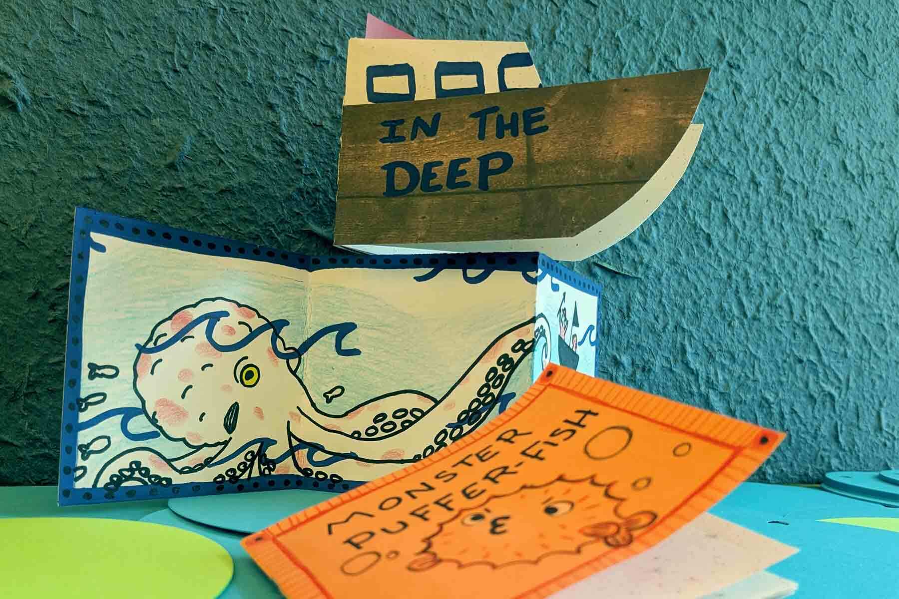 A picture of 3 zines depicting an octopus, puffer-fish and one shaped like a boat