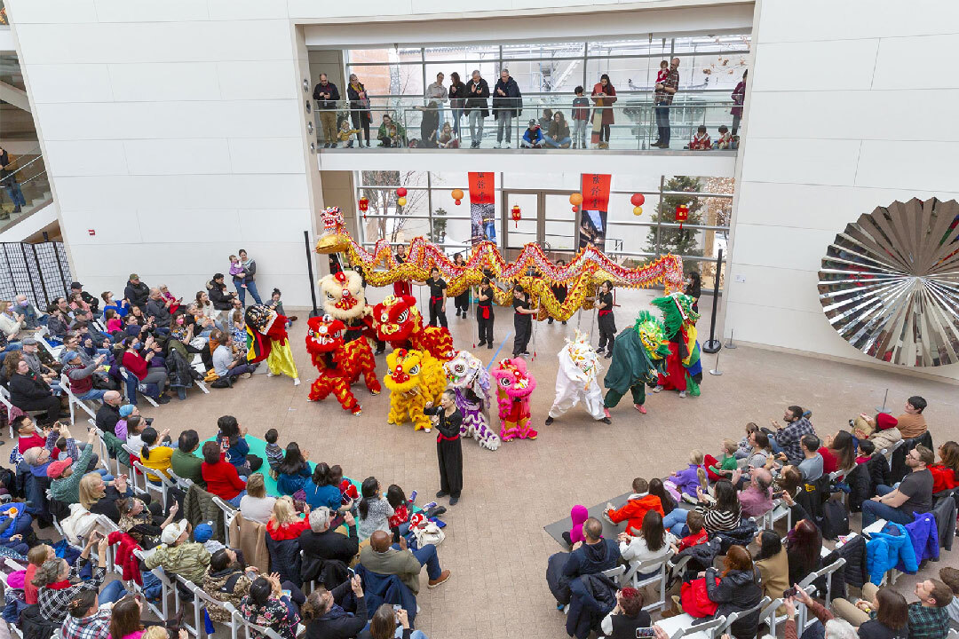 Lion and dragon dancers perform in a crowded indoor atrium as audiences watch from below and above
