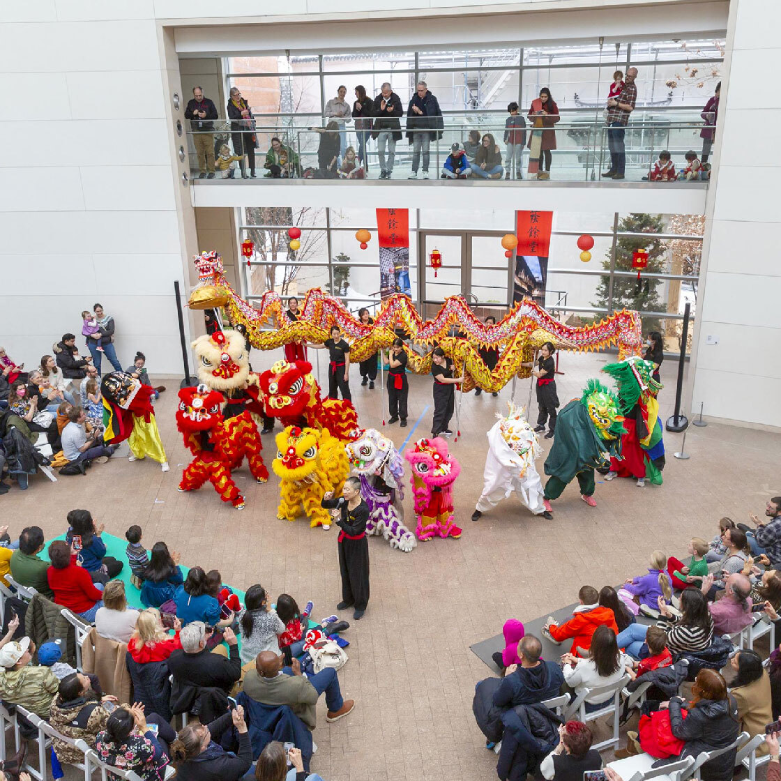 Lion and dragon dancers perform in a crowded indoor atrium as audiences watch from below and above