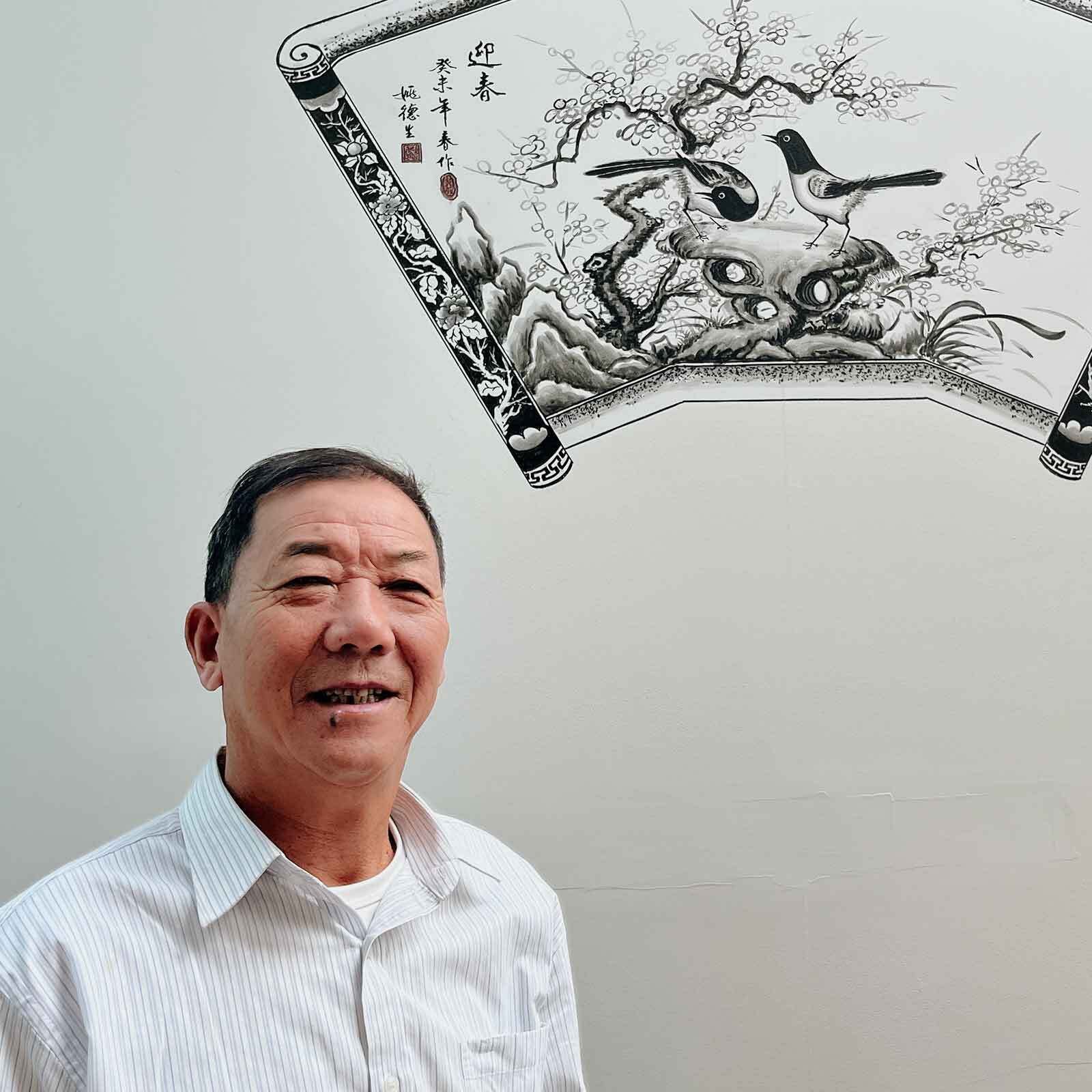 Artist Yao Desheng with one of his paintings on Yin Yu Tang: A Chinese Home's exterior, 2026. Peabody Essex Museum. Photo by Yao Wu/PEM.