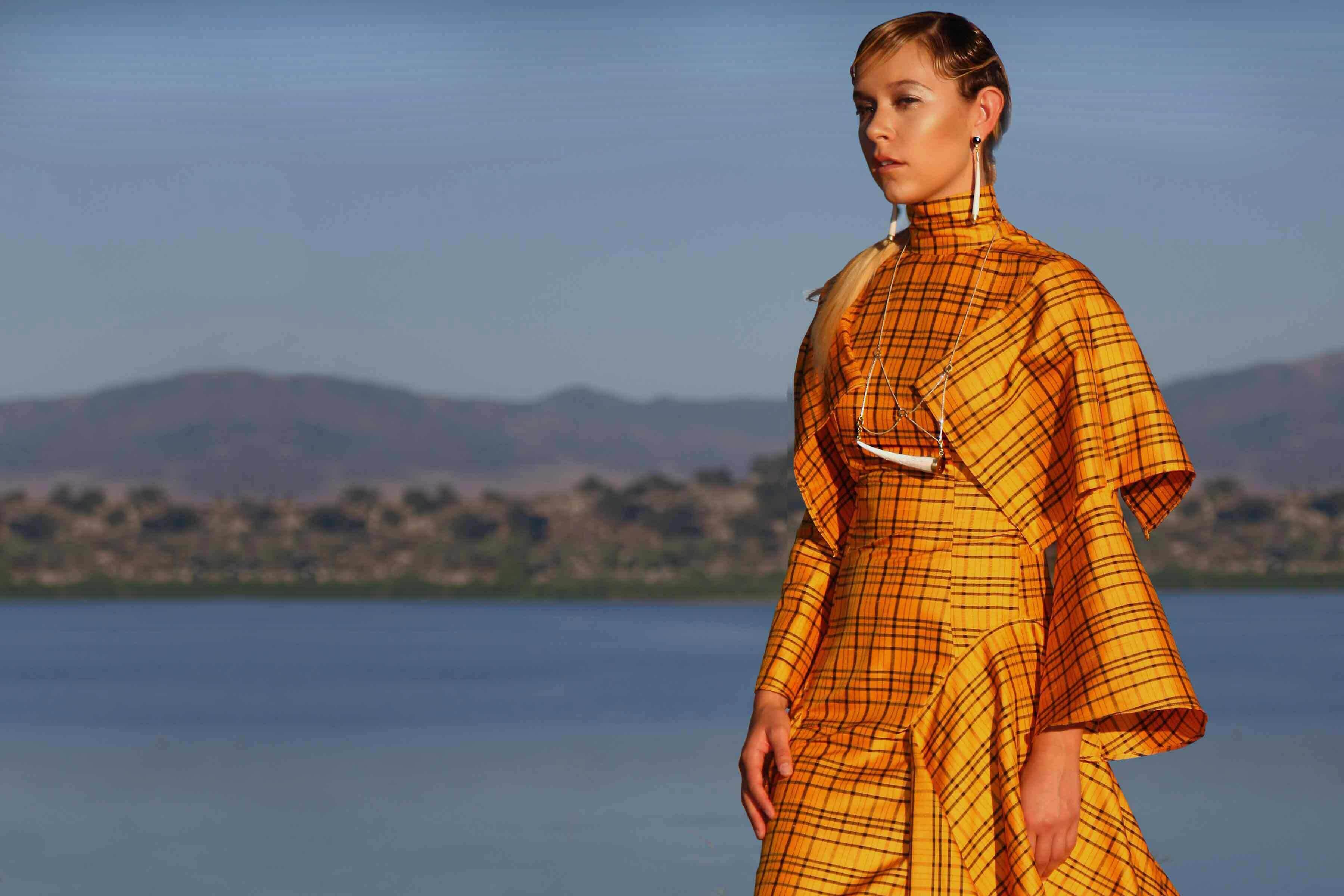A woman wearing a golden plaid dress in front of a lake with the oceans in the background