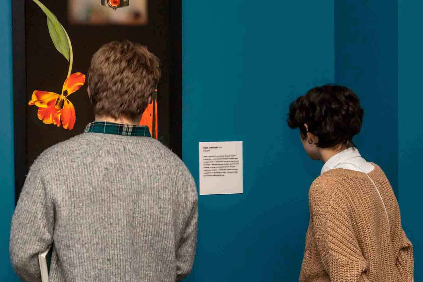 Visitors in a gallery looking at artwork of flowers on a blue wall