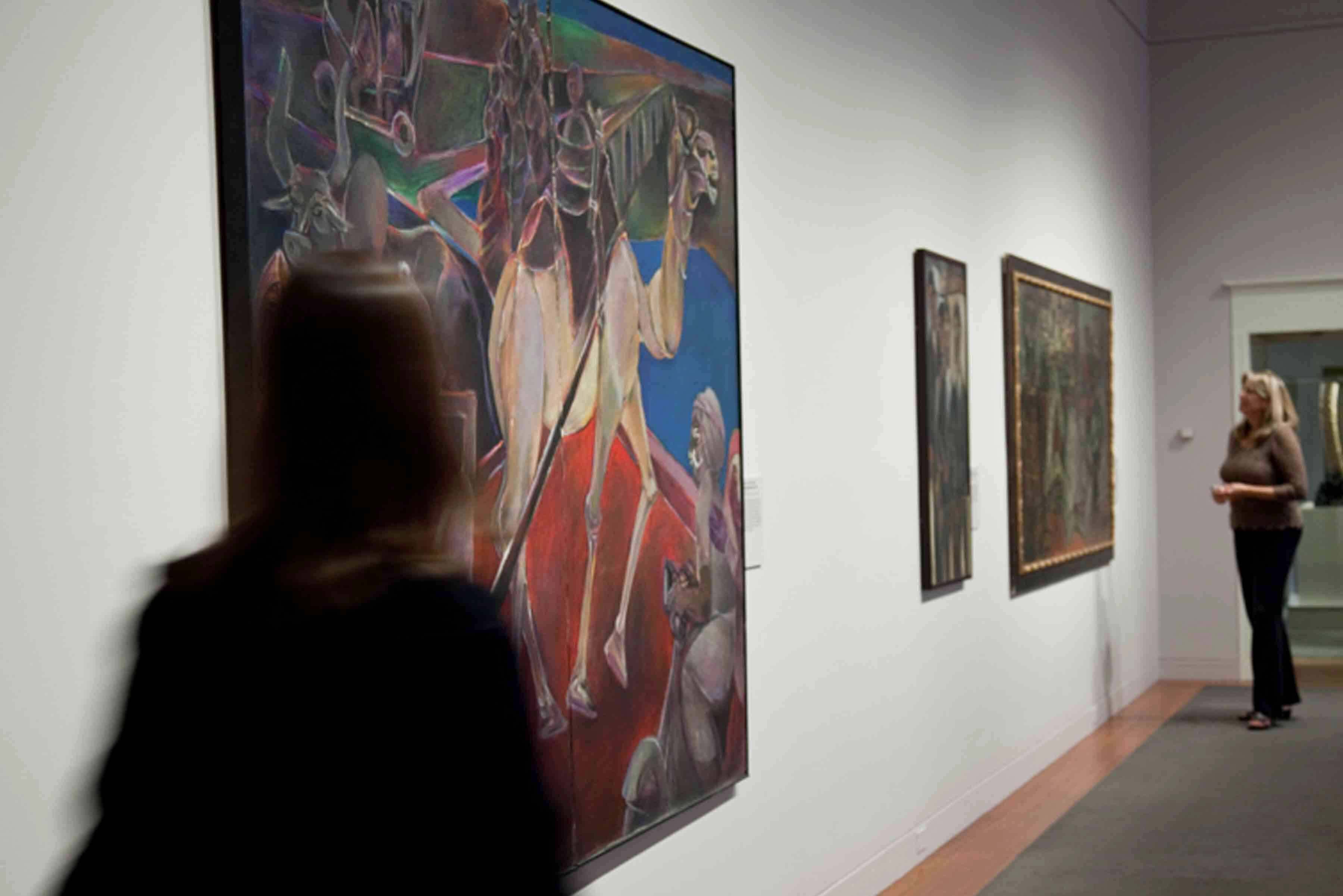 Visitors looking at paintings on a wall in the gallery