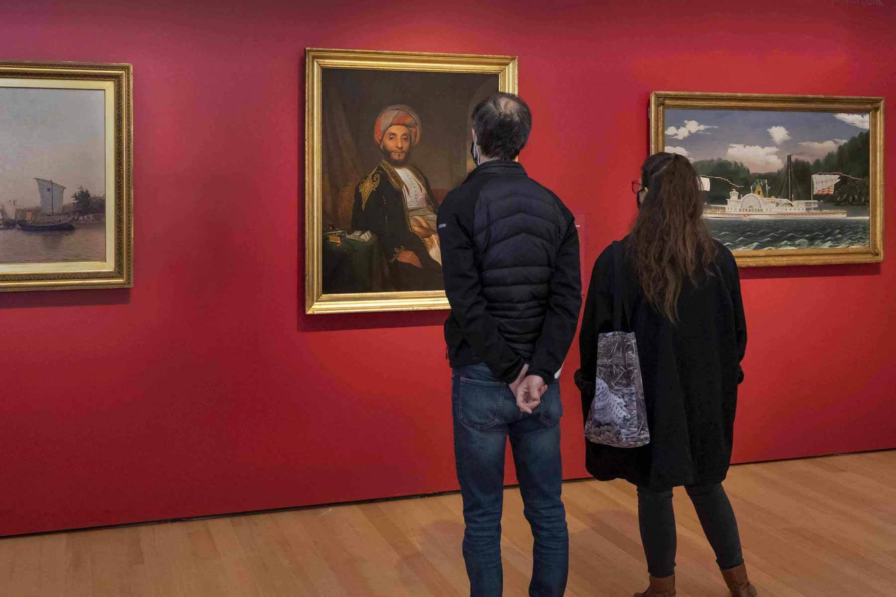A man and woman looking at paintings hanging on a deep red wall.