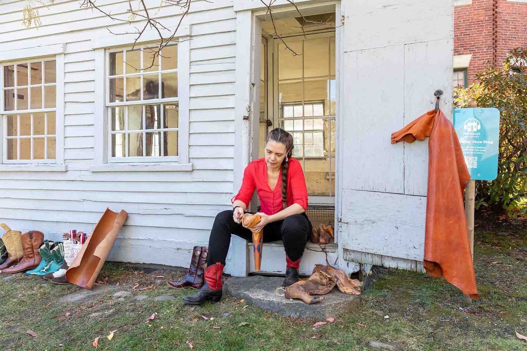 Person sitting in a doorway shaping a piece of leather outside a historic building.