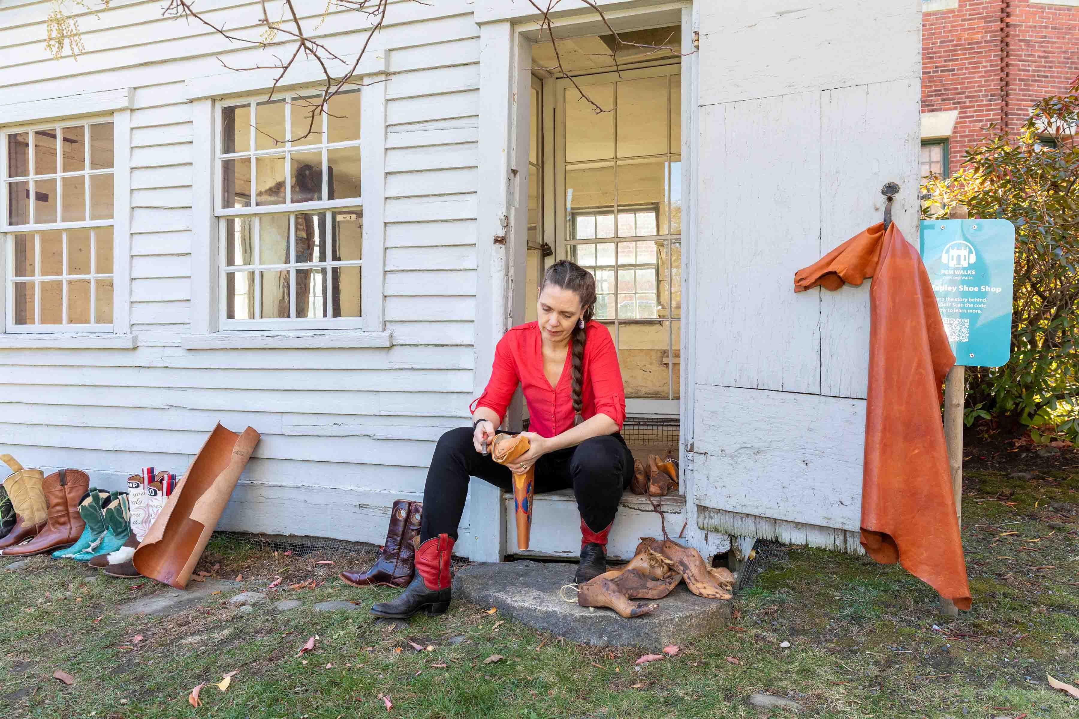 Person sitting in a doorway shaping a piece of leather outside a historic building.